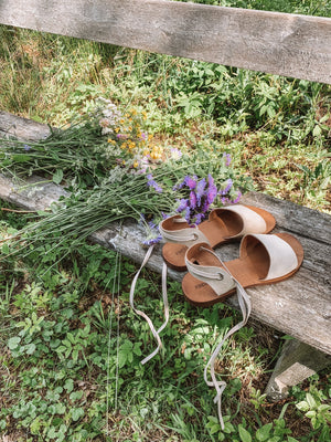 Acapulco beige vegan sandals placed on wooden bench with wildflowers in nature, sustainable summer footwear for women