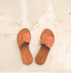 Top view flat lay of Cali vegan sandals in cognac with rose lace detail on stone background