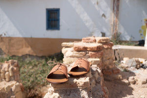 Cali vegan sandals in cognac with rose lace detail placed on stone wall in Mediterranean outdoor setting
