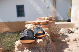 Cali vegan sandals in gravel blue with lace detail placed on stone wall in Mediterranean outdoor setting