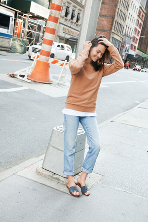 Woman wearing Cali vegan sandals in gravel blue styled with jeans and sweater in urban street setting