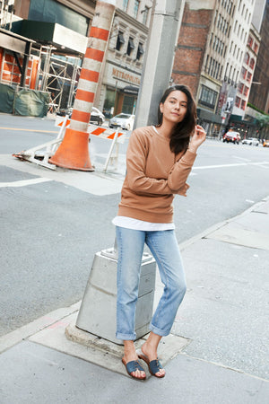 Woman wearing Cali vegan sandals in gravel blue styled with jeans and sweater posing in urban street setting