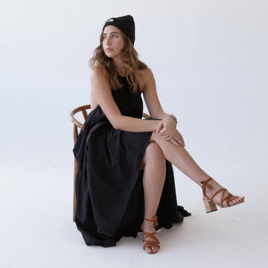 Woman wearing Camila Plus vegan lace up heels with brown ribbons styled with black dress sitting on chair in minimal studio setting