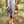Woman holding vegan lace up sandals with neutral ribbons while walking barefoot in nature with flowers, sustainable lifestyle