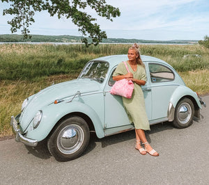 Woman wearing vegan lace up sandals styled with green dress standing by vintage car during summer road trip in Europe