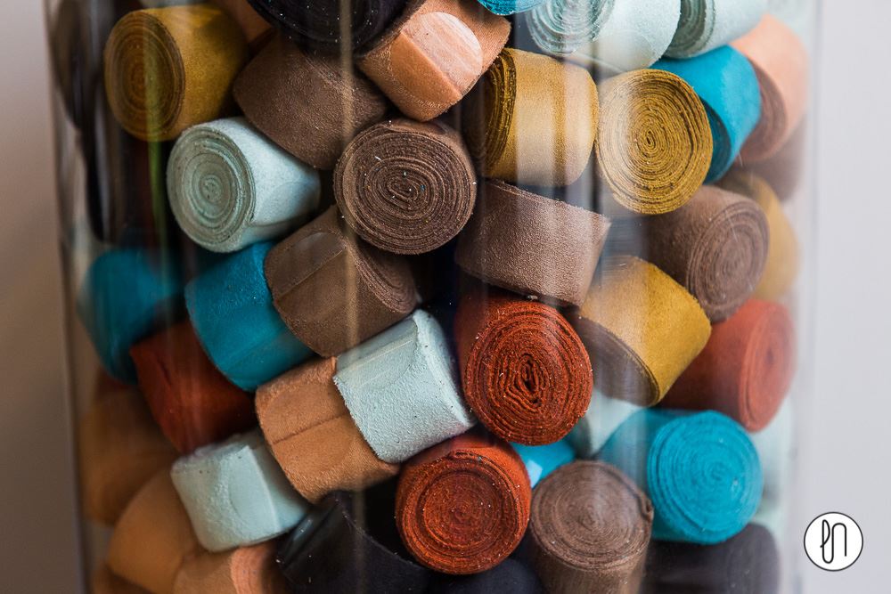 A glass jar filled with neatly rolled colorful ribbons in shades of turquoise, brown, mustard, and coral — ready to be used for Rarámuri sandals.