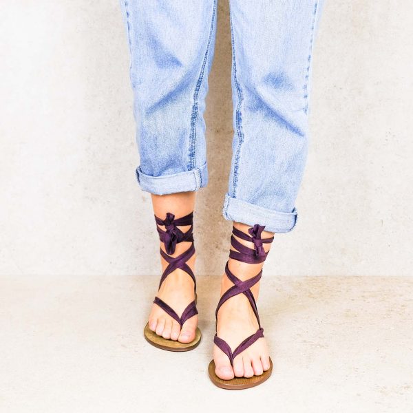 Close-up of feet in Rarámuri flat sandals with purple ribbon ties, styled with rolled-up blue jeans.